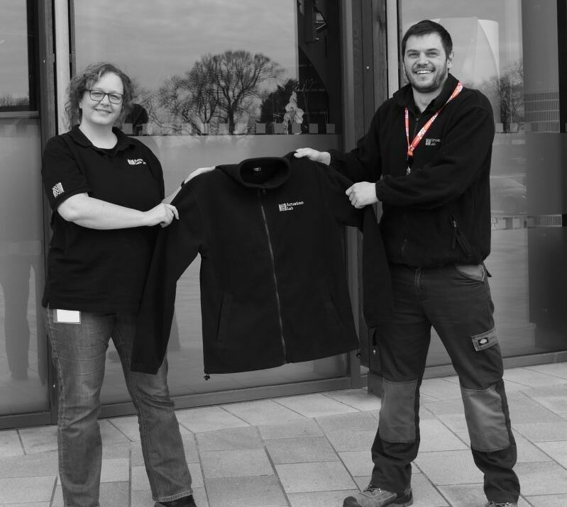 Photo of our Head of R&D Tom handing Gaelle, our new admin, her Actuation Lab fleece